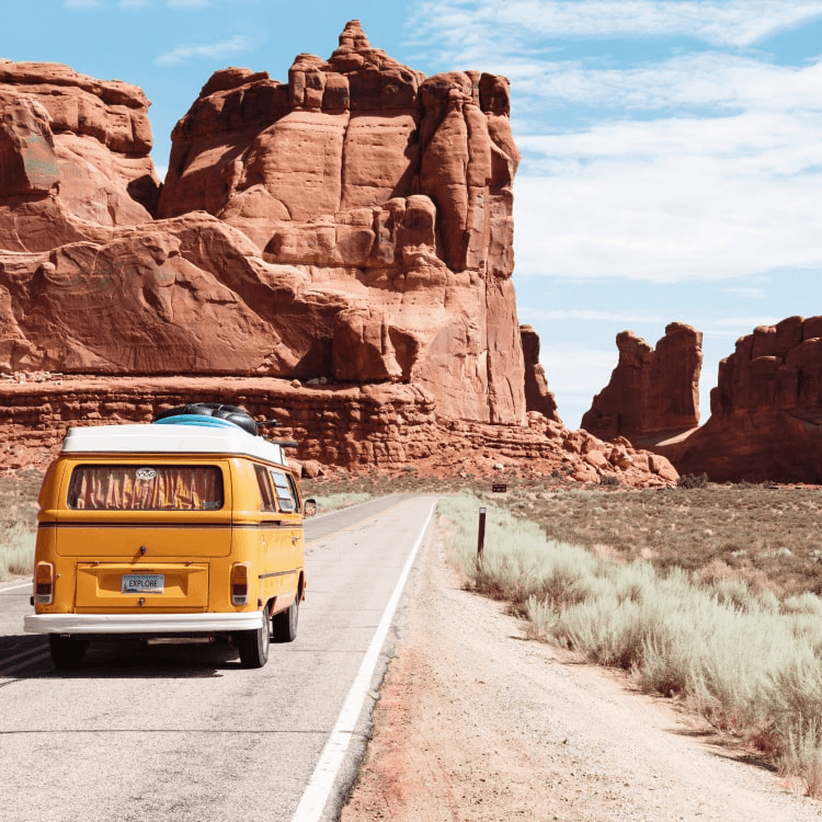 A yellow wan driving down the road in a scenery full of rock mountains.